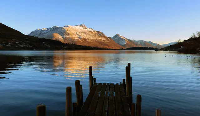 A wooden jetty on the Frankton Arm of Lake Wakatipu, with hills across the still water.