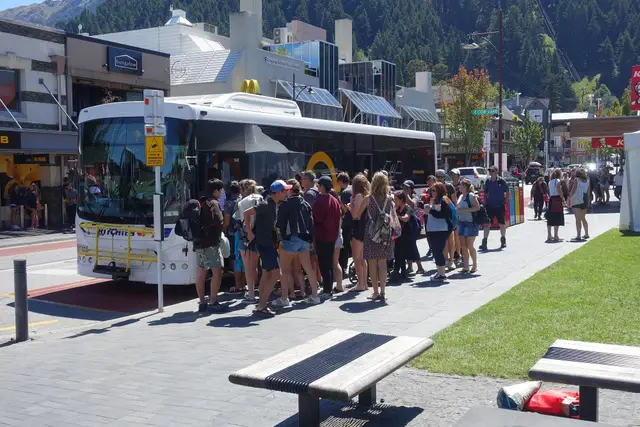A yellow Orbus bus at a Queenstown stop, with a queue of passengers boarding through the front door.