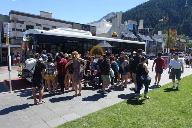Passengers boarding a yellow Orbus bus at a Queenstown stop.