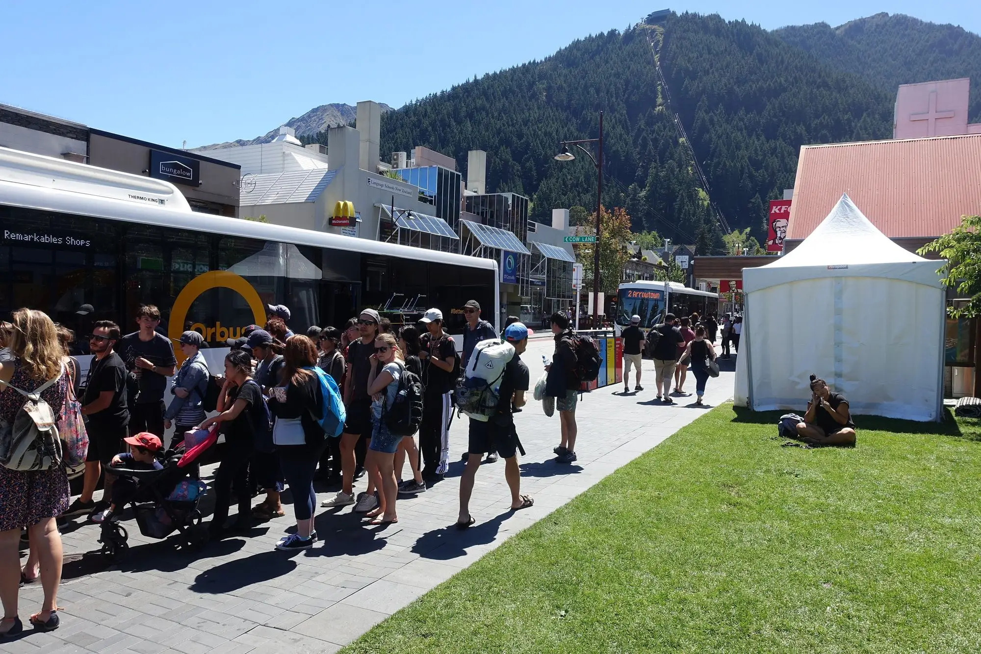 A yellow Orbus bus stopped in Queenstown, with passengers at the doors.