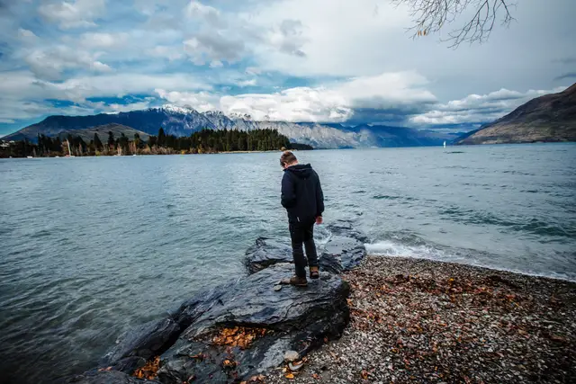 The rocky shoreline of Lake Wakatipu at Queenstown, with a person standing on the rocks.