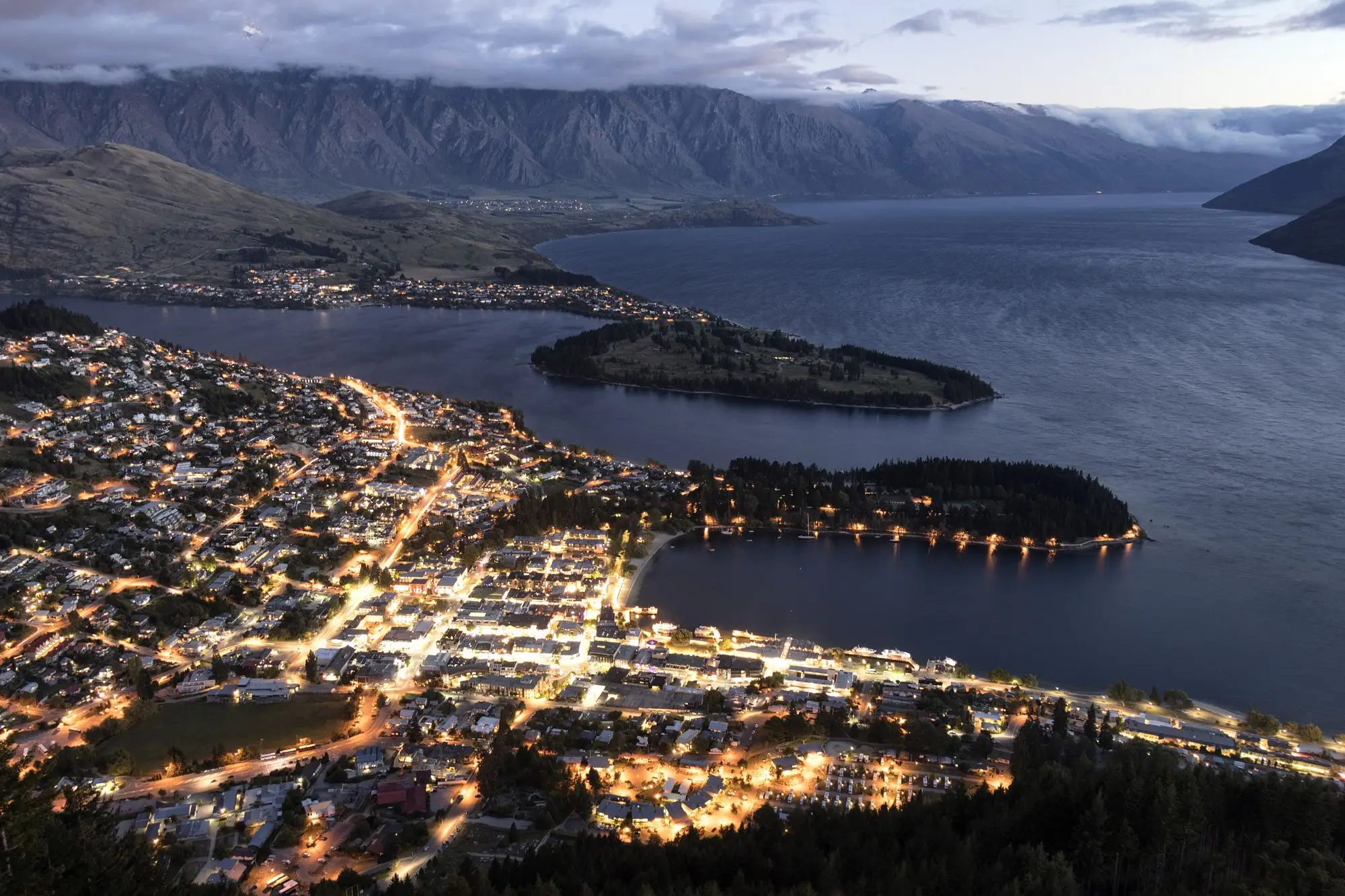 Queenstown and Lake Wakatipu at night, seen from above, with streets and the lakefront lit.