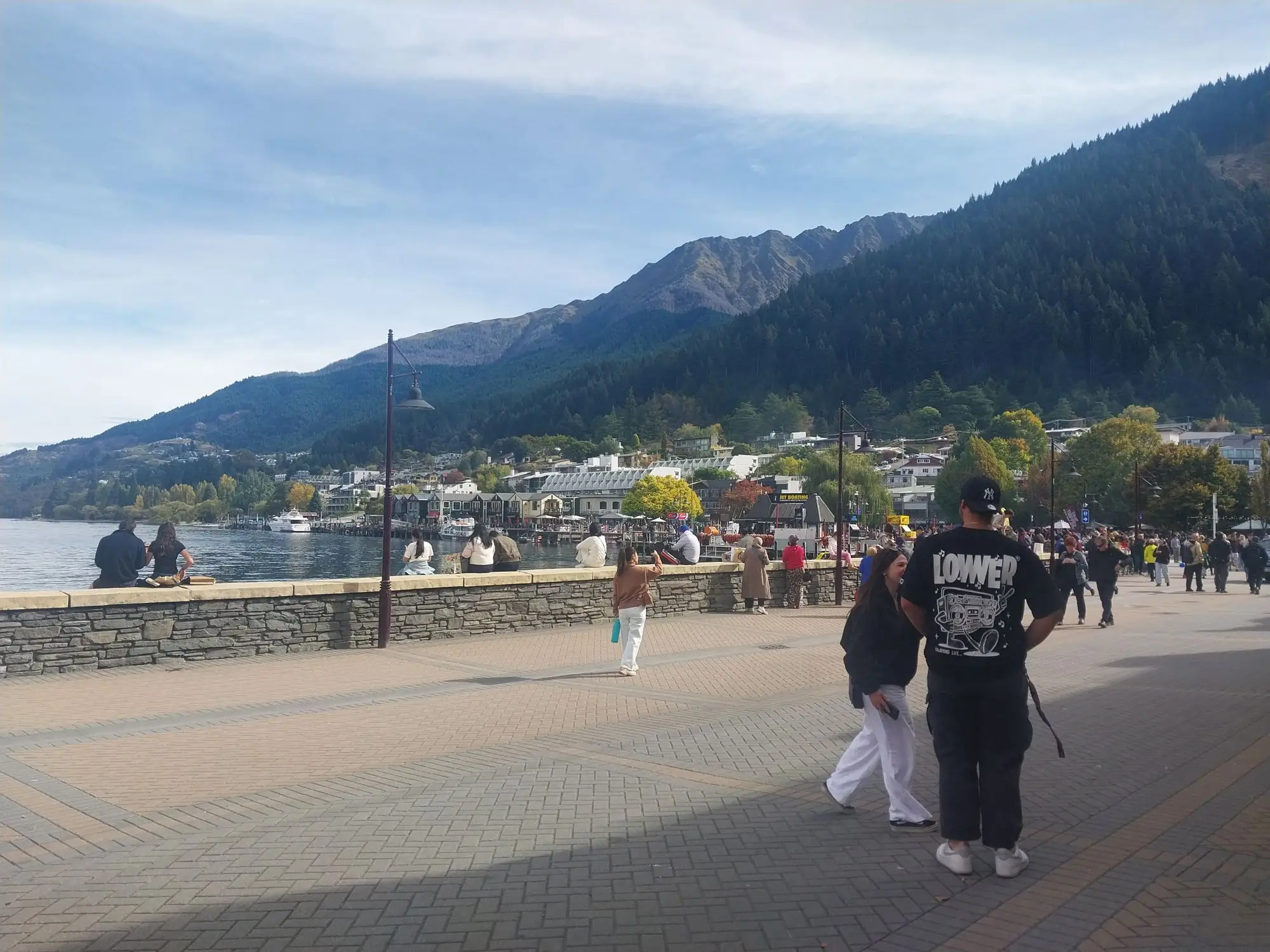 A Queenstown town-centre street in April 2026, with people walking between shops and a bus at the kerb.