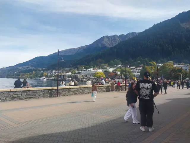 A Queenstown town-centre street in April 2026, with people walking between shops and a bus at the kerb.